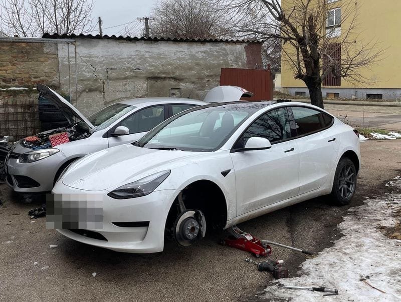 Fehér Tesla Model 3 kerékcsere közben a műhely udvarán, emelőn
