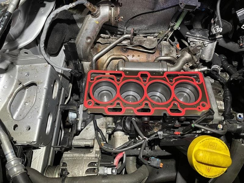 Új, fém fejtömítés piros tömítőcsíkokkal a megtisztított motorblokkon